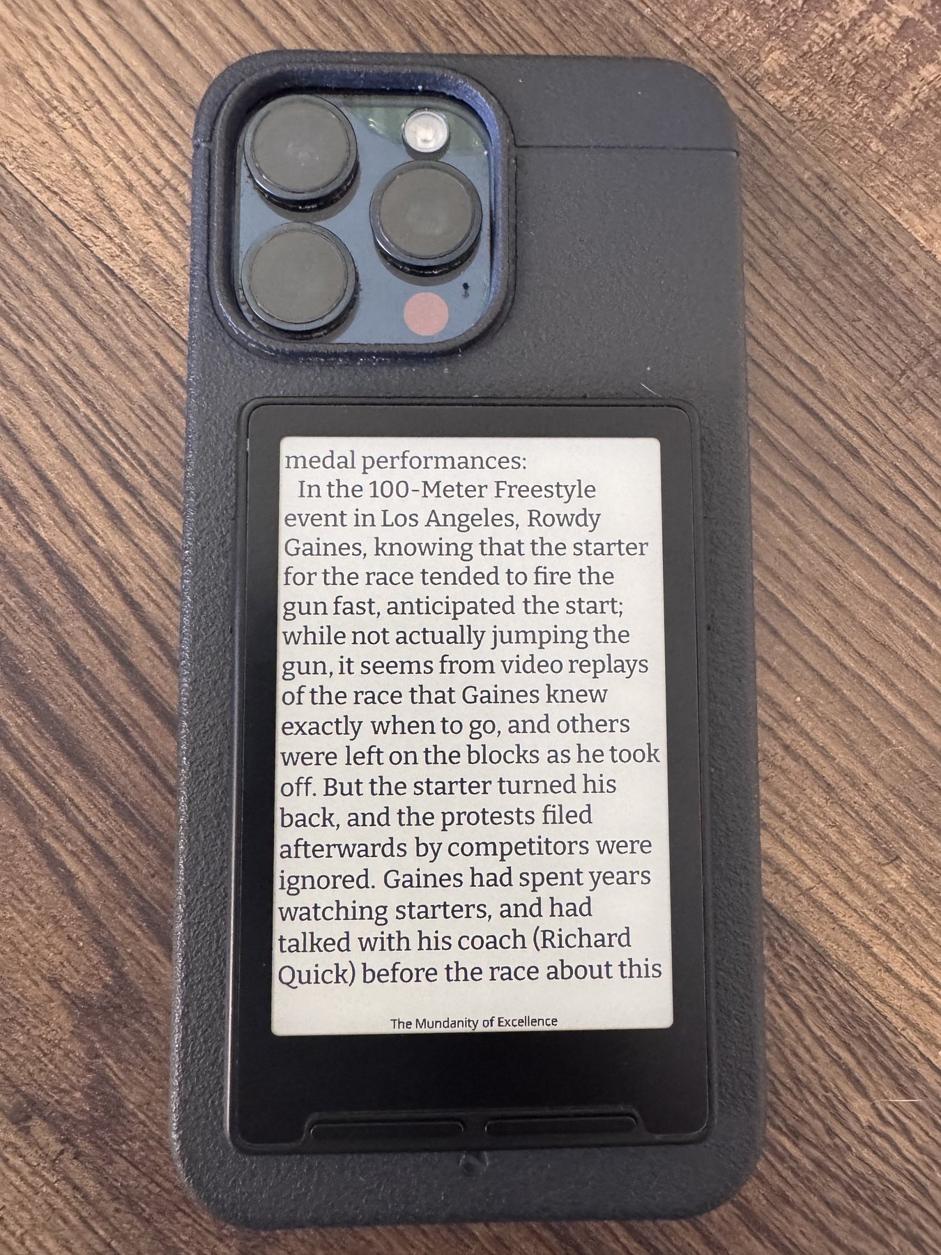The Xteink e-reader attached to the back of a phone and displaying text from a saved long-form article